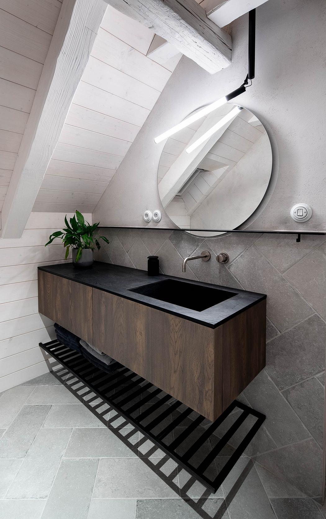 Modern bathroom with a slanted ceiling, round mirror, and black sink vanity.