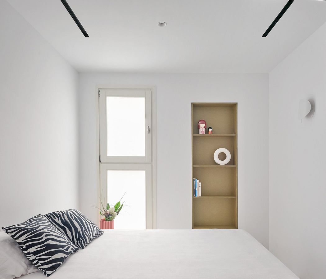 Minimalist bedroom with white walls, a small window, and a built-in shelf
