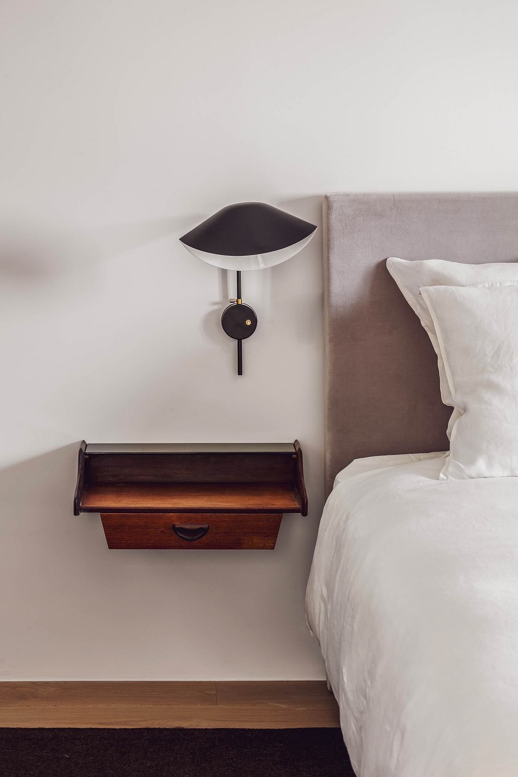 Minimalist bedroom detail with a wall-mounted bedside lamp and wooden drawer.
