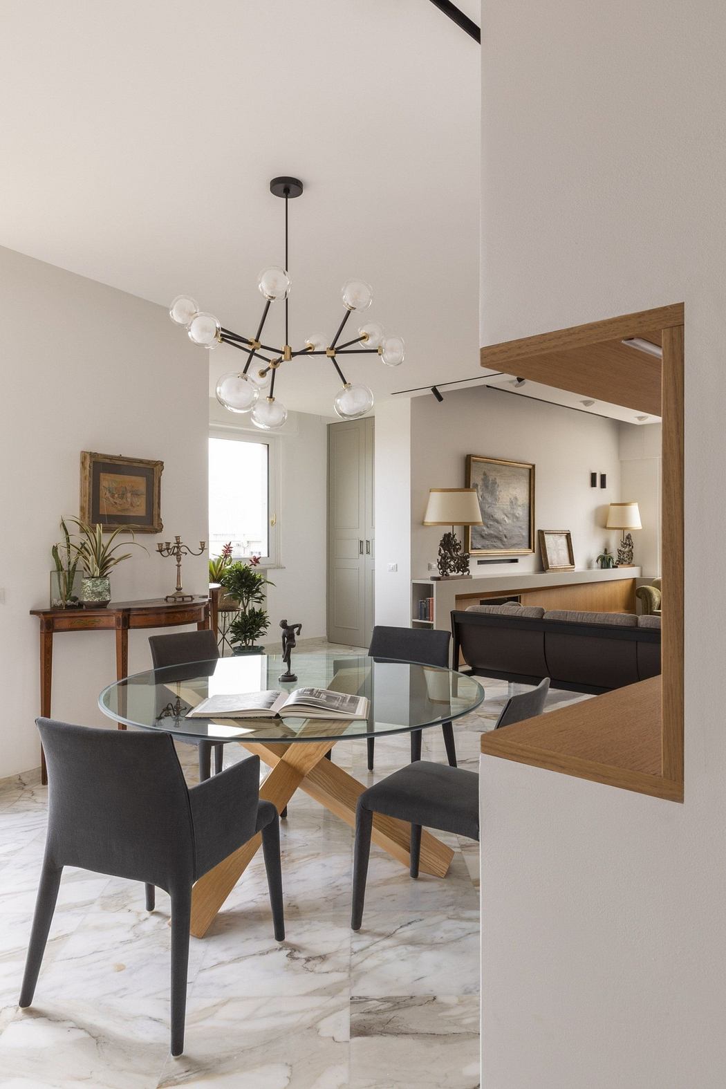 Elegant dining space with glass table, unique chandelier, and marble flooring.
