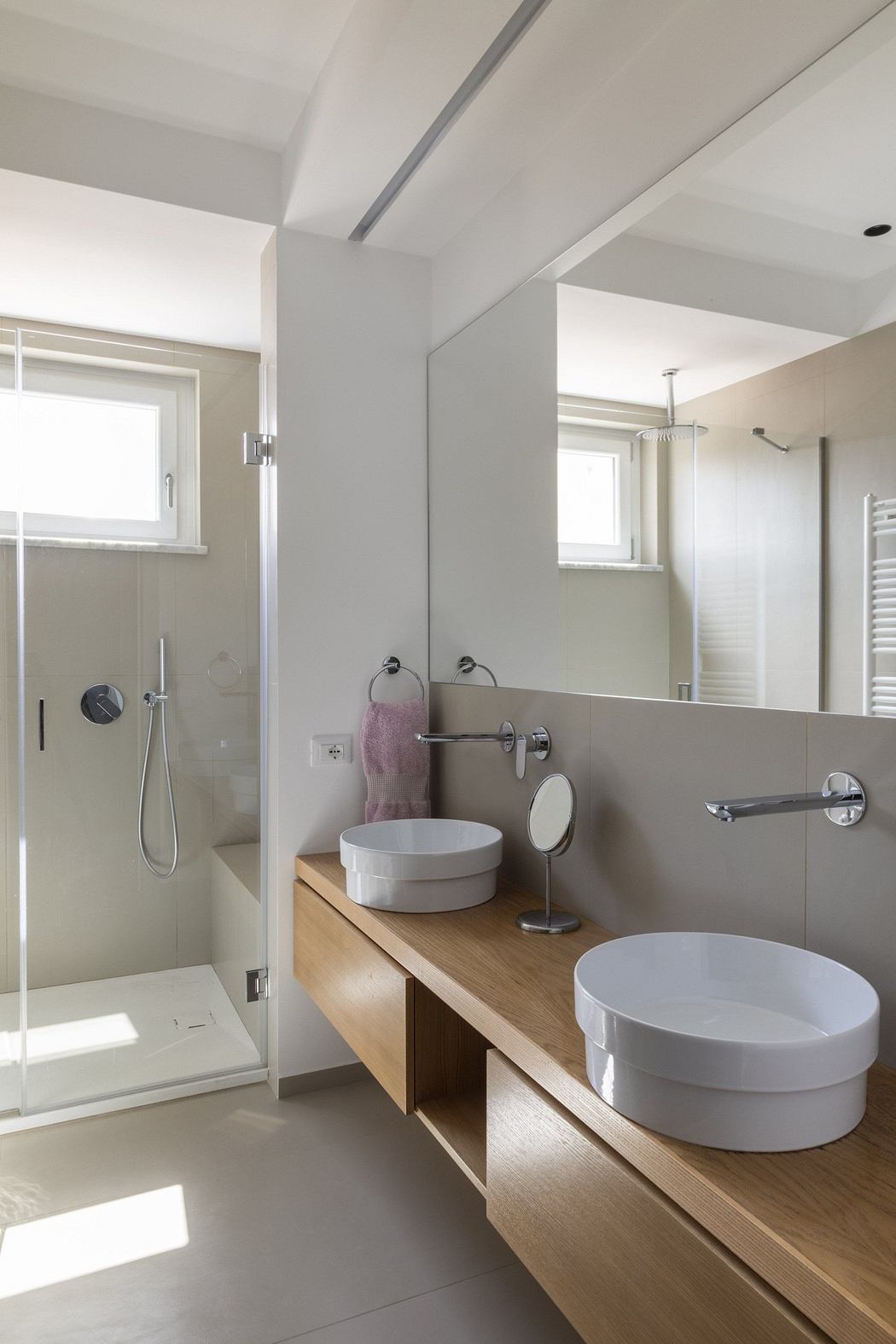 Modern bathroom with wooden vanity, two sinks, and a glass shower enclosure.