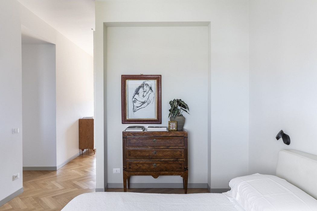 Minimalist bedroom with vintage wooden dresser and framed artwork.