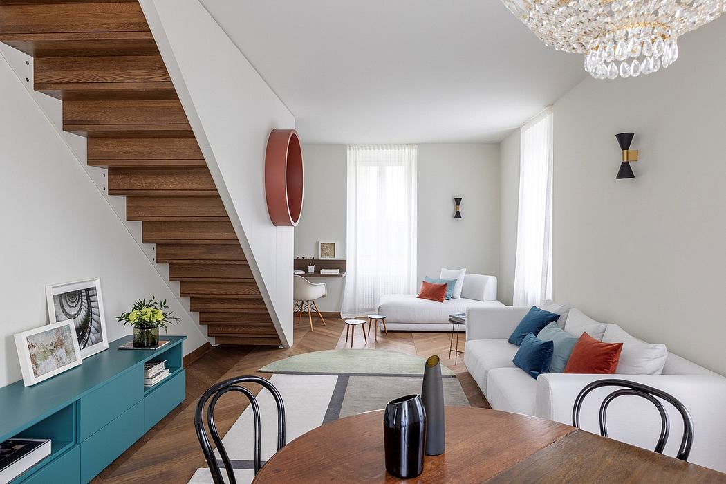 Inviting open-concept living space with modern wooden stairs, vibrant colors, and a chandelier.