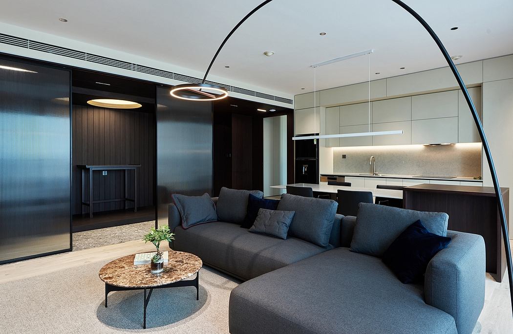 Sleek, modern living room with curved lighting fixture, dark furniture, and open kitchen.