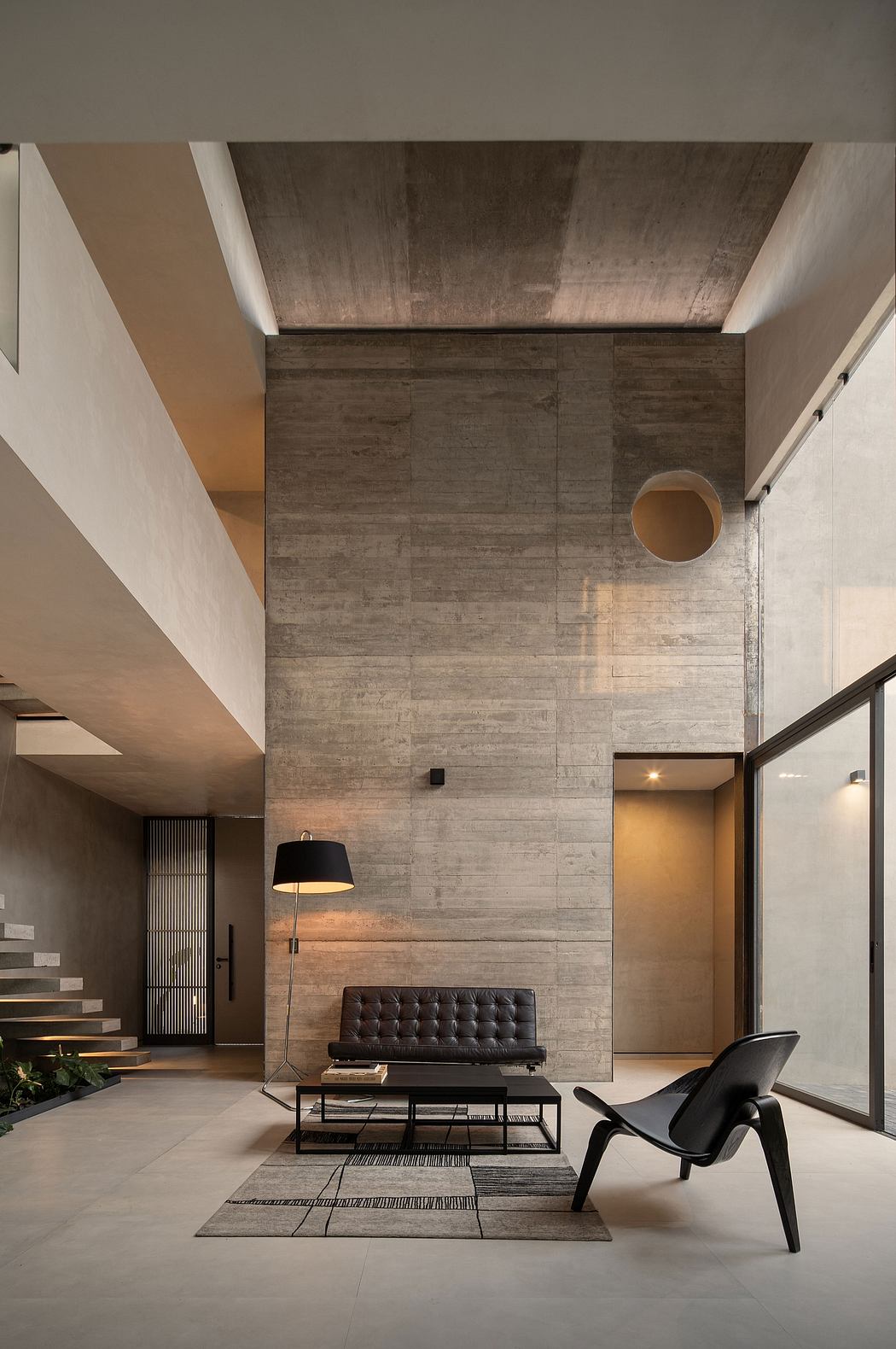 Modern interior with high ceiling, concrete walls, staircase, and designer furniture.