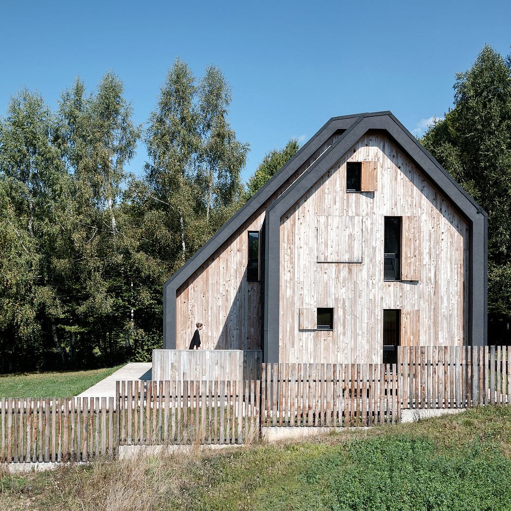 A rustic cabin with an angular roof, wooden facade, and a fence surrounding the property.