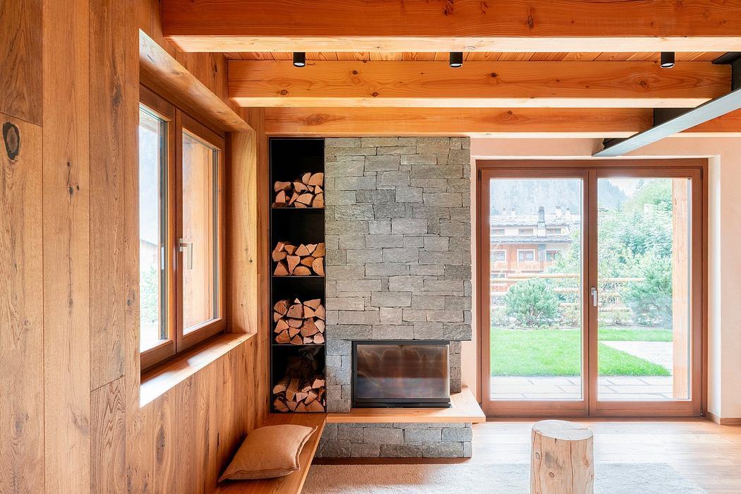 Rustic wooden interior with stone fireplace and firewood storage, overlooking a garden.