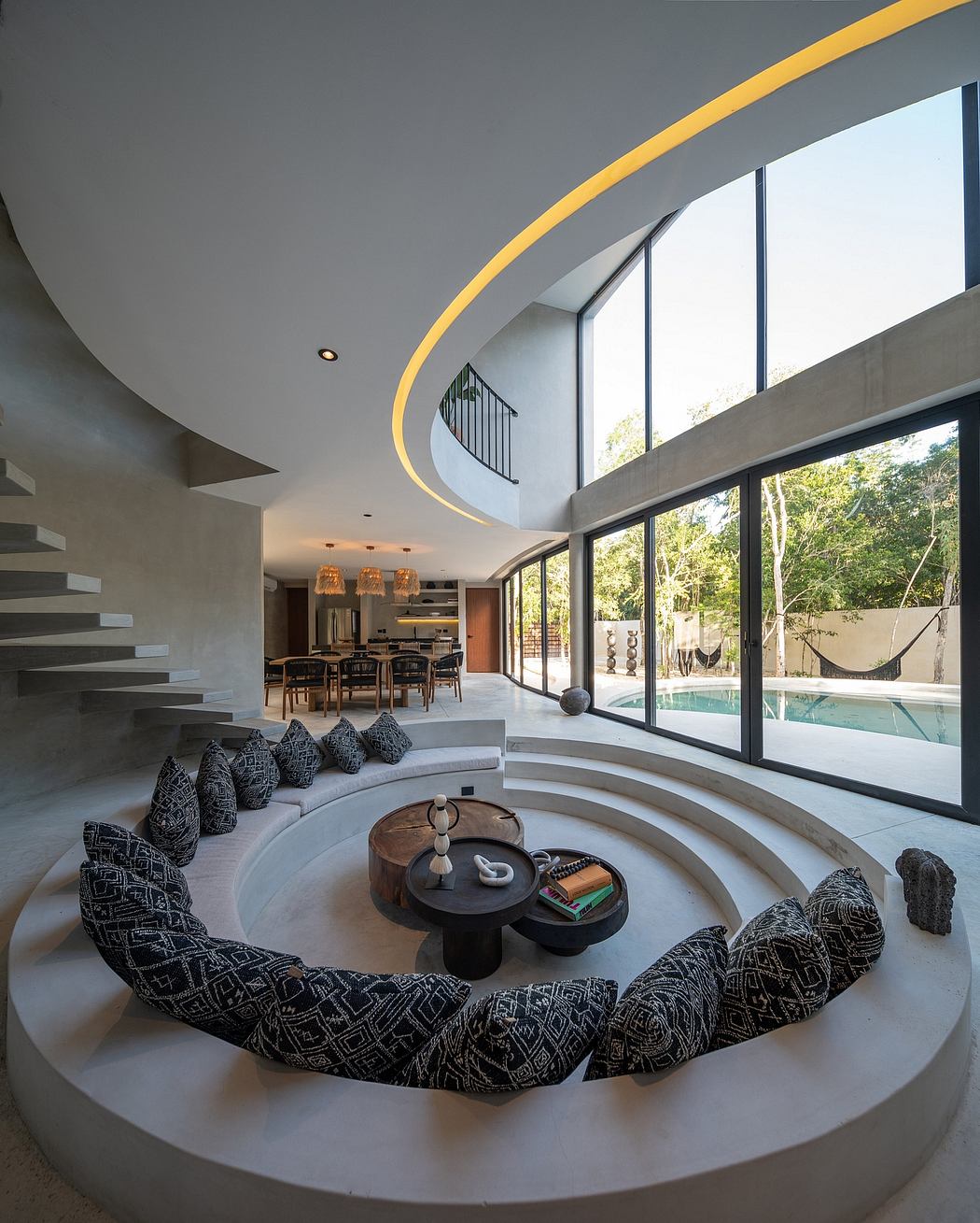 Modern living room with circular seating, sleek staircase, and large windows.