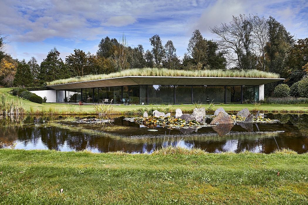 Modern glass building with grass roof reflected in a pond.