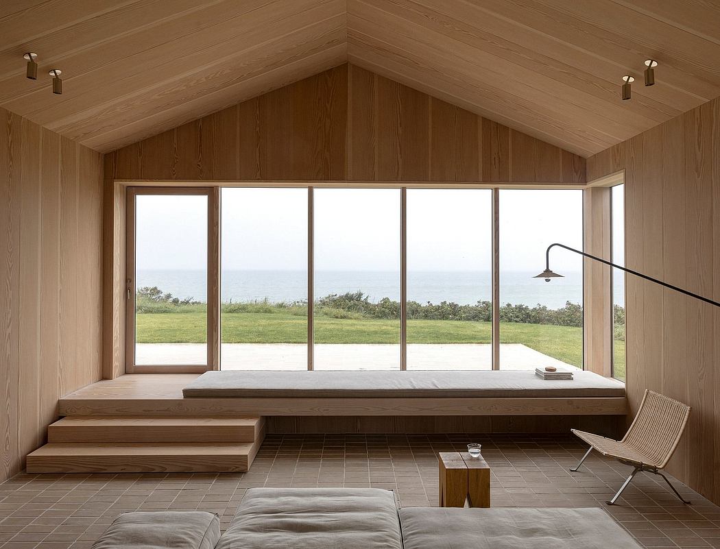Minimalist wooden interior with large window overlooking the sea.