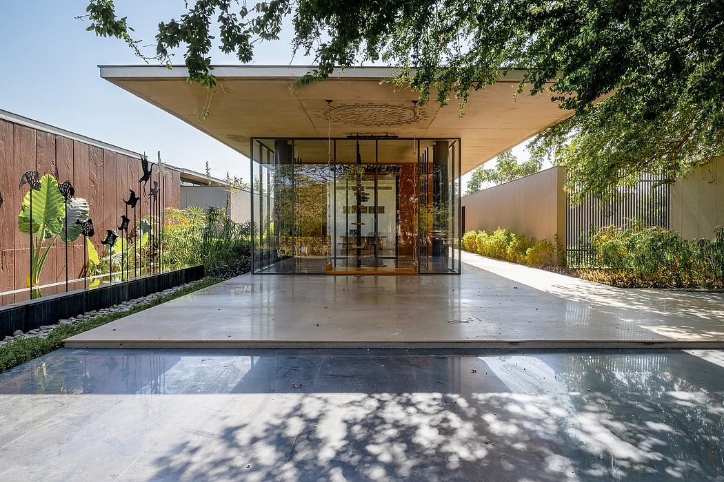 A modern home with an open glass entryway, covered by an overhanging roof and surrounded by lush greenery.