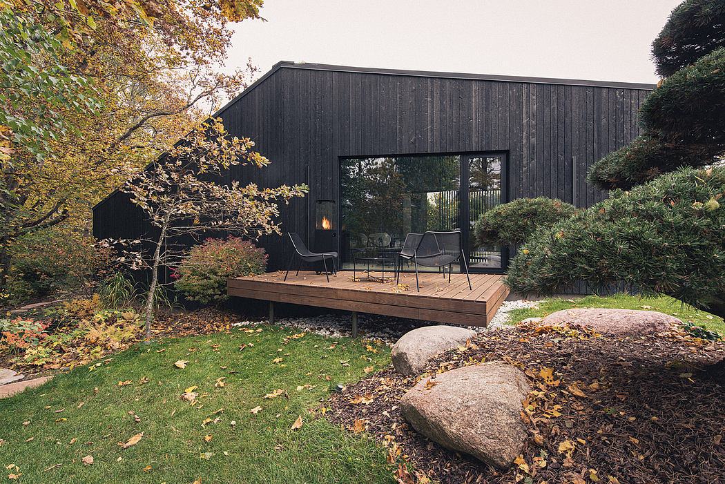 A cozy, modern cabin in an autumn forest, with a wood deck, chairs, and a fireplace.