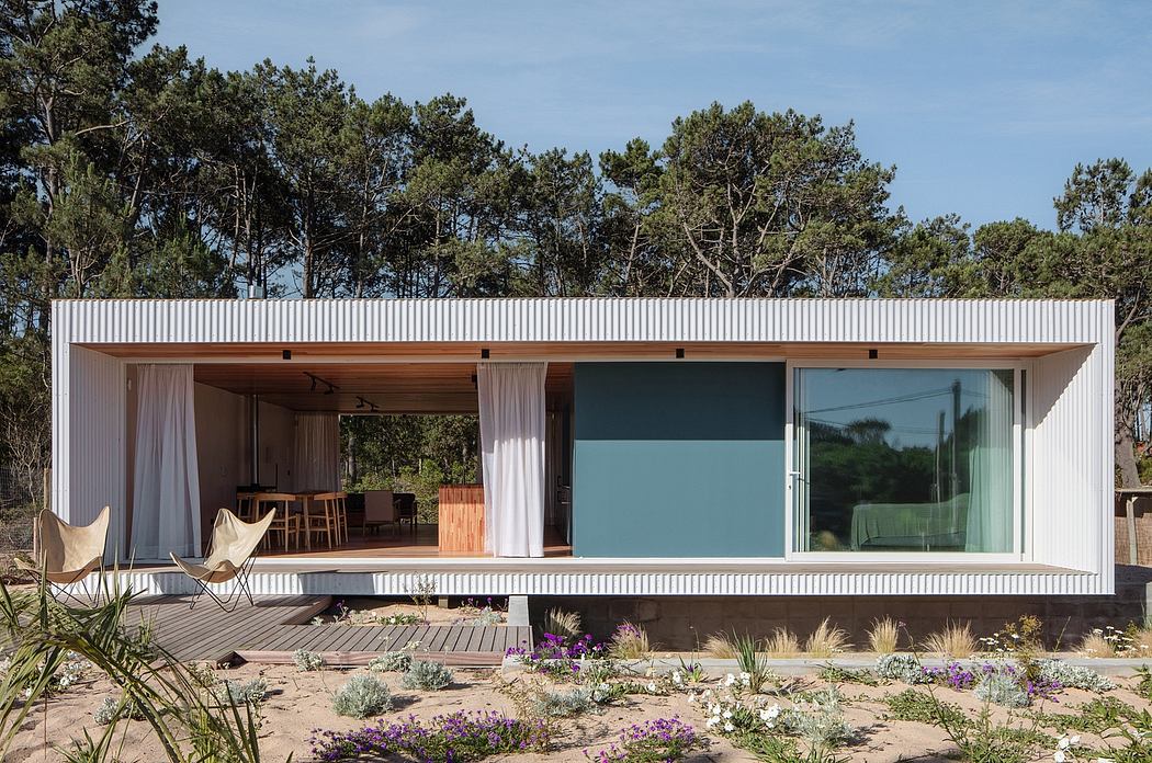 Modern minimalist house with large windows and wooden deck surrounded by natural landscape.