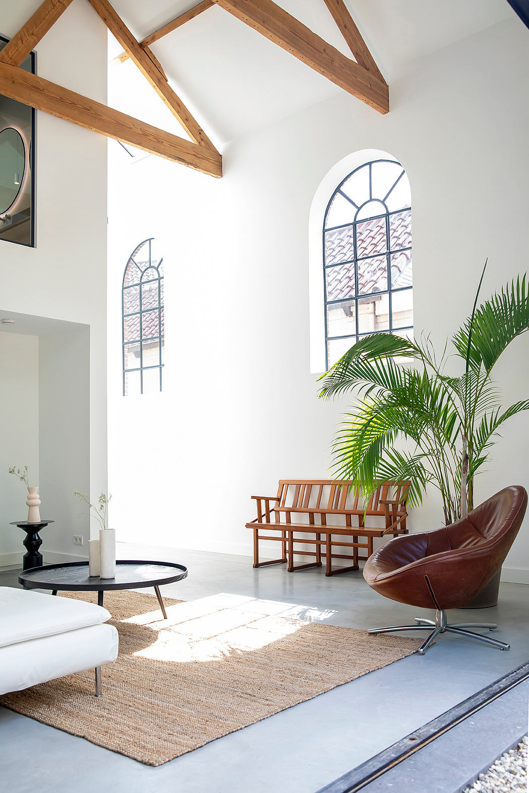 Spacious living area with arched windows, wooden beams, and tropical plants.