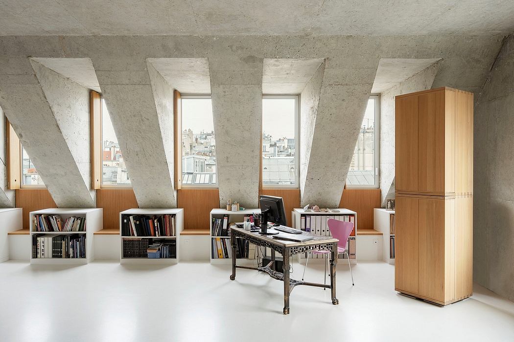 A modern, minimalist office space with concrete walls, angled windows, and built-in wooden storage.