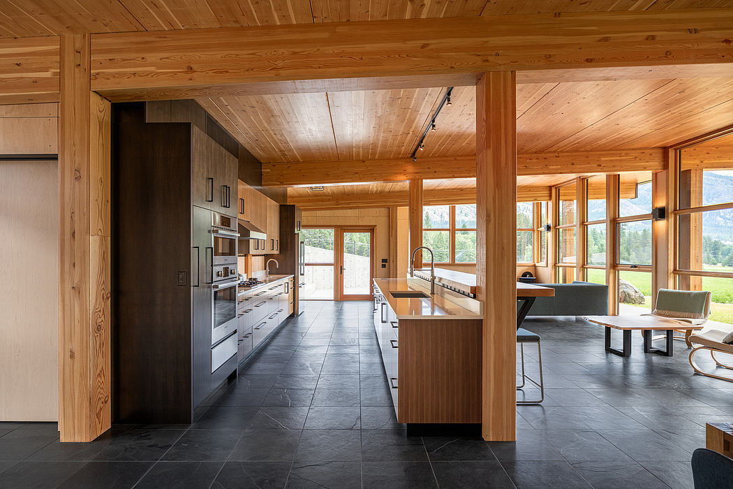 Spacious modern kitchen with wooden beams, sleek cabinets, and large windows overlooking nature.