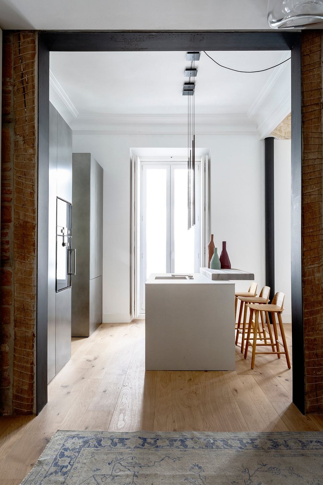 An open, minimalist kitchen with a central island, wooden floors, and a modern light fixture.