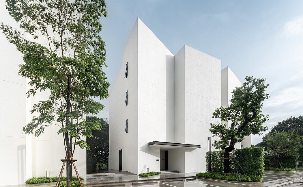 Modern white building with geometric design and surrounding greenery.
