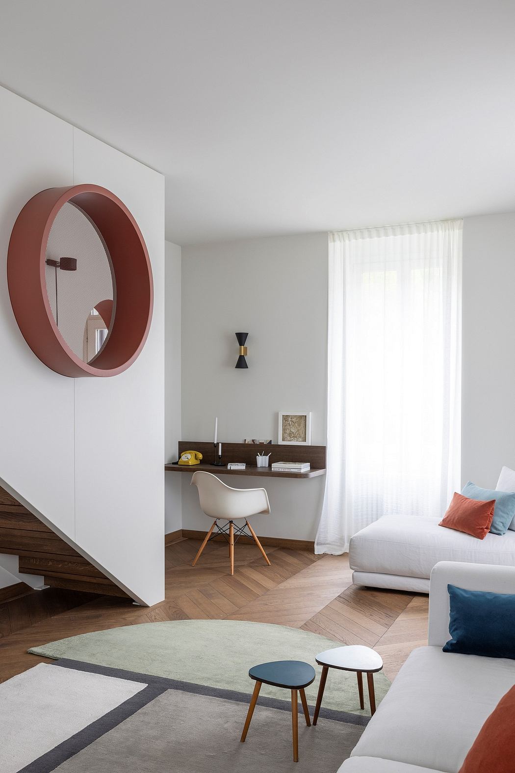Minimalist living room with circular wall mirror, built-in desk, and wood floors.