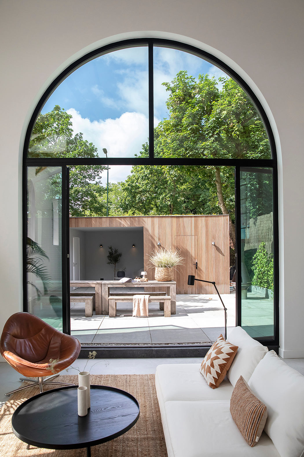 Spacious, modern living room with arched glass doors overlooking a lush outdoor patio.