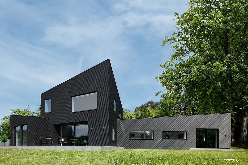 A modern black-clad house with large windows overlooking a grassy lawn and trees.