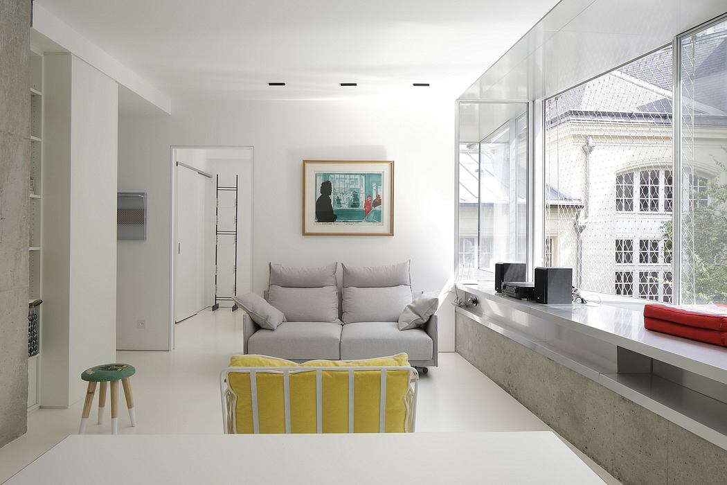 Minimalist living room with gray sofa, yellow chair, and large window overlooking exterior.