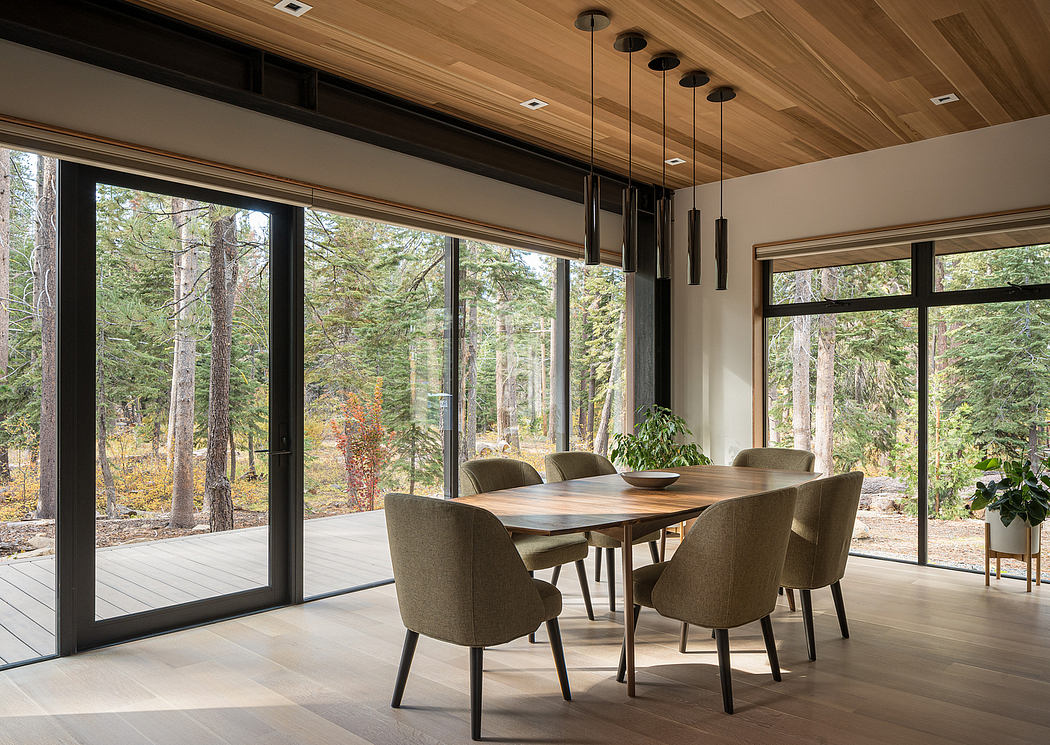 Contemporary dining room with large windows overlooking a forest.
