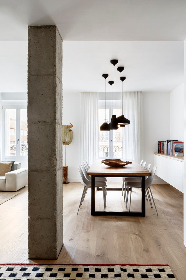 Minimalist dining room with exposed concrete pillar and designer pendant lights.