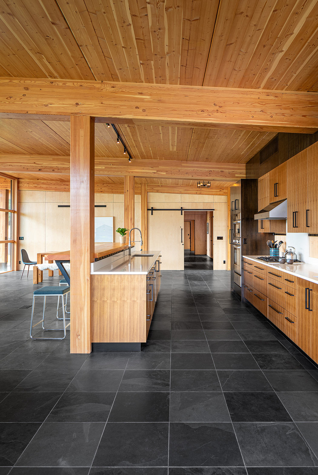 A modern kitchen with a wooden ceiling, slate tiles, and a central island with wooden countertops.