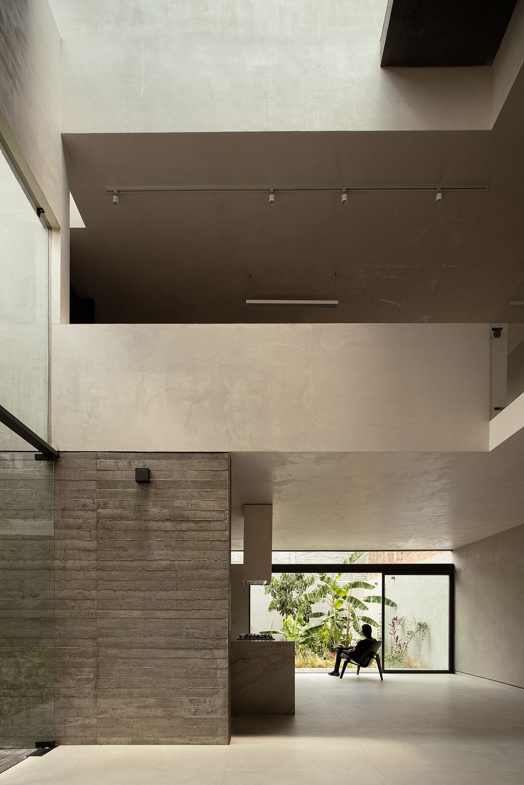 Modern interior with high ceilings, concrete walls, and a person sitting by a large