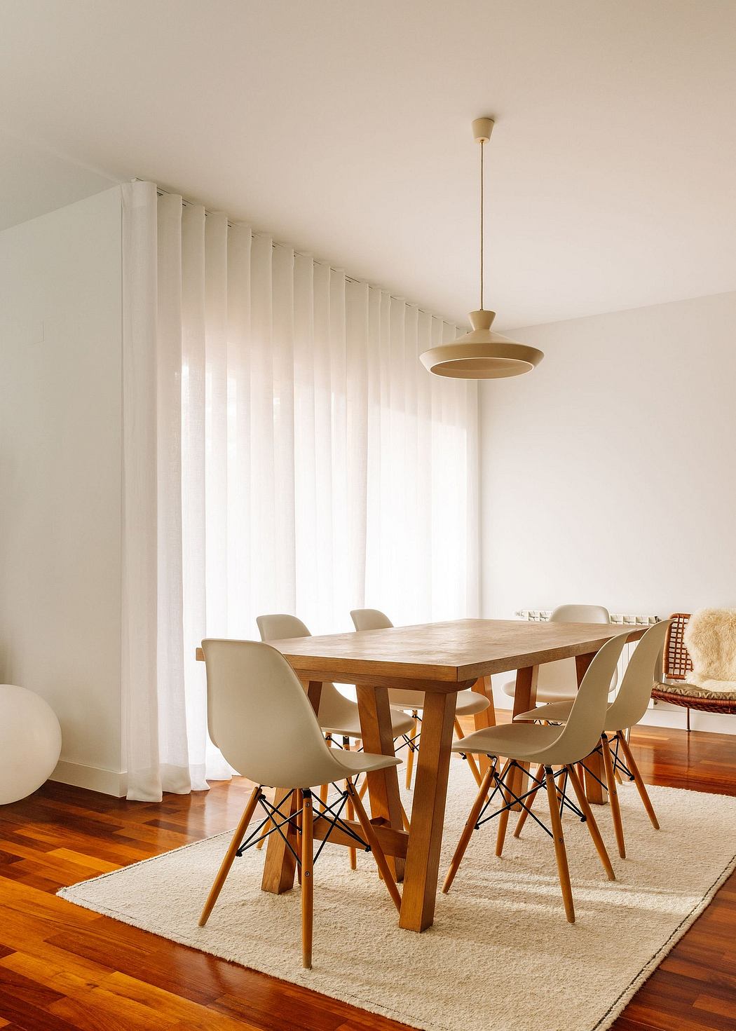Minimalist dining room with wooden table, Eames-style chairs, pendant light, and curtains.
