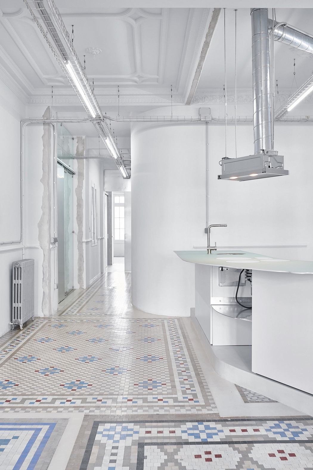Expansive white hallway with ornate ceiling, industrial lighting, and patterned tile floor.
