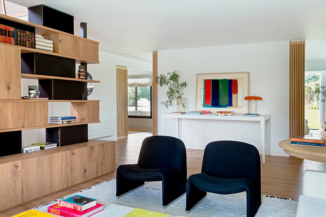 A modern, open-concept living space with wooden shelving, plush chairs, and vibrant artwork.