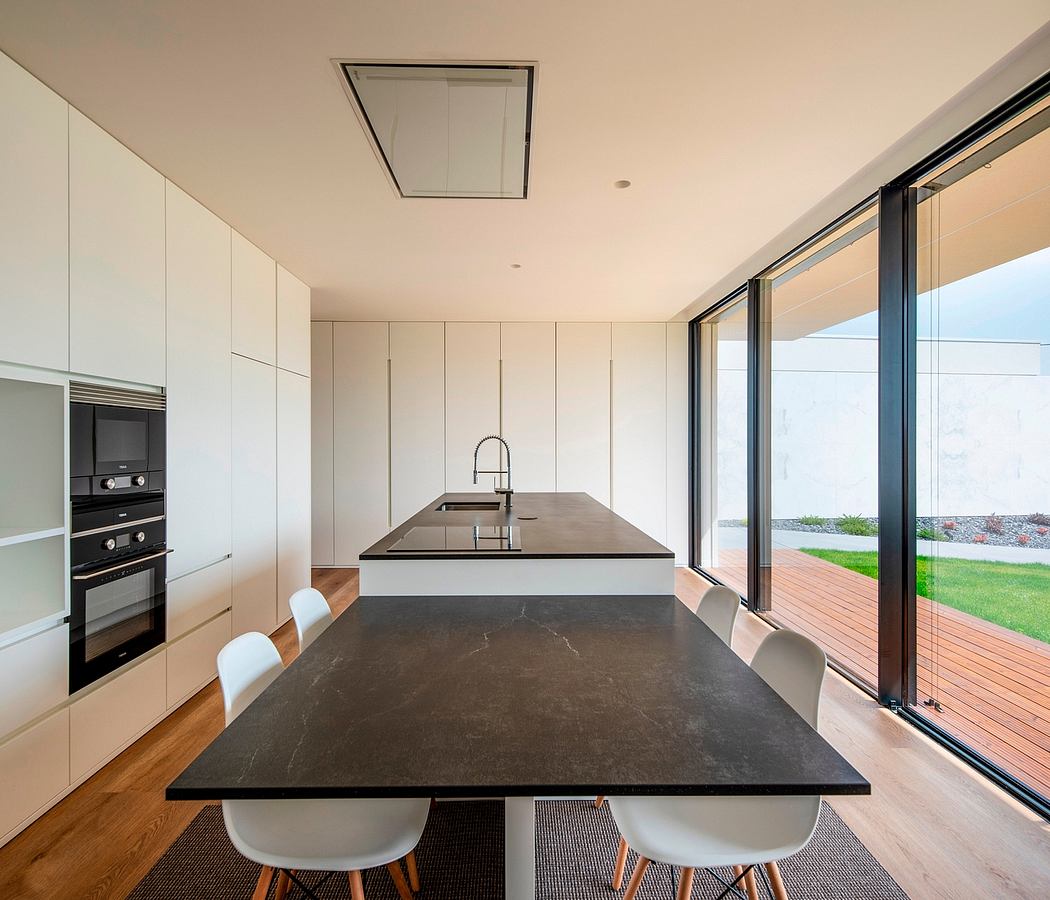 Modern kitchen with large island, built-in appliances, and glass wall.
