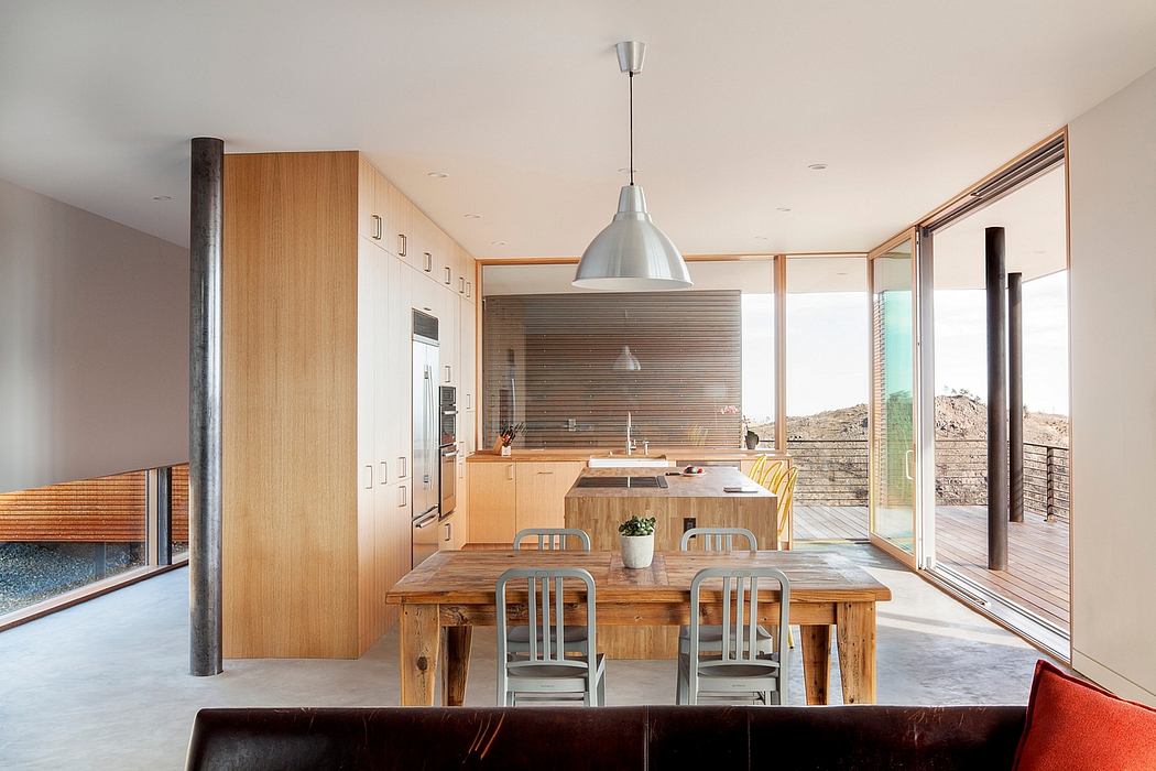 Modern kitchen with wooden table, cabinets, and large windows.