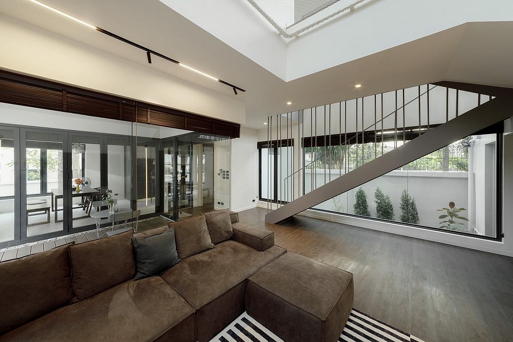 Modern living room with sectional sofa, high ceiling, staircase, and large windows.