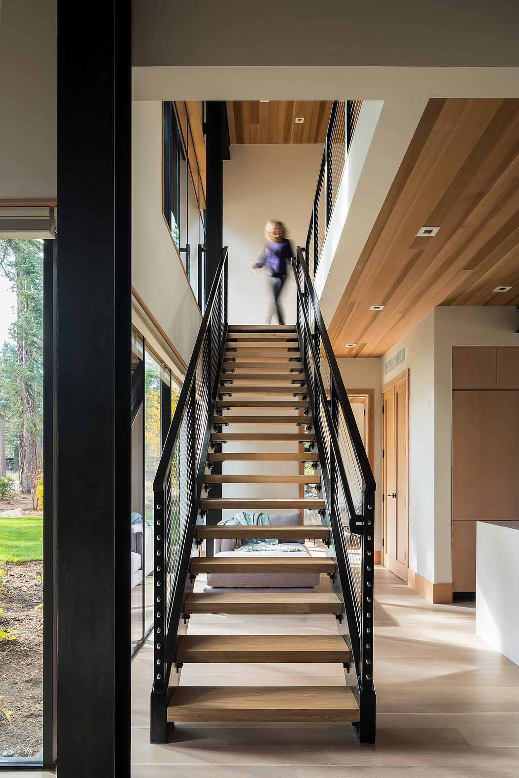 Modern staircase with a person descending, wood accents, and large windows.