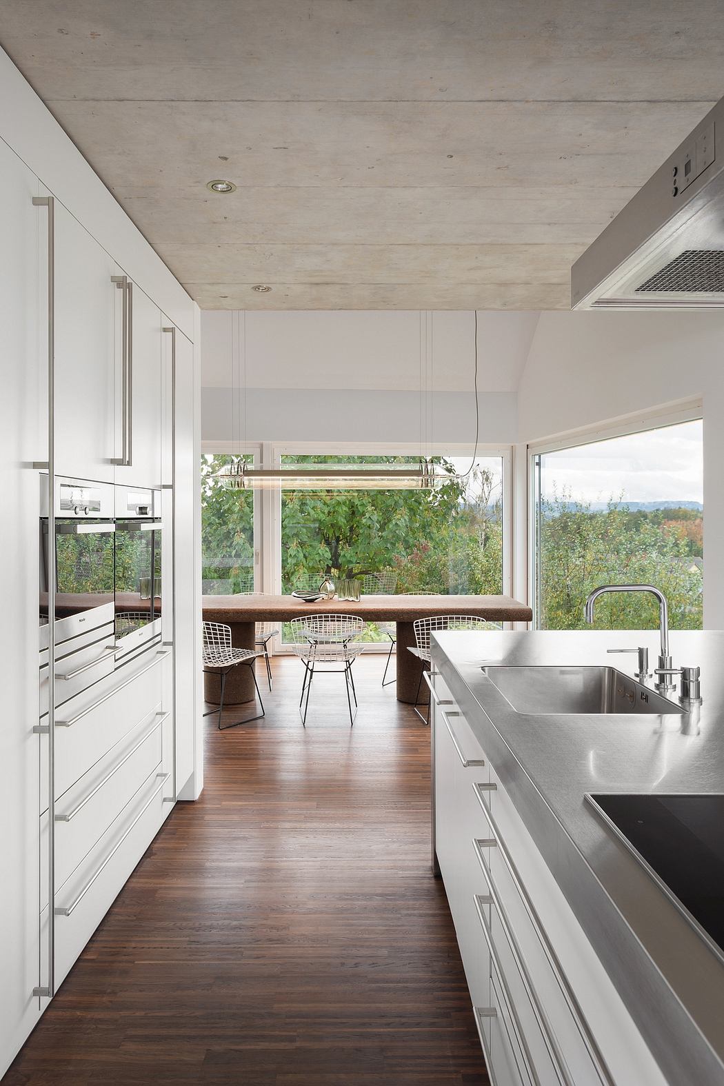 Sleek modern kitchen with stainless steel appliances, concrete ceiling, and scenic views.
