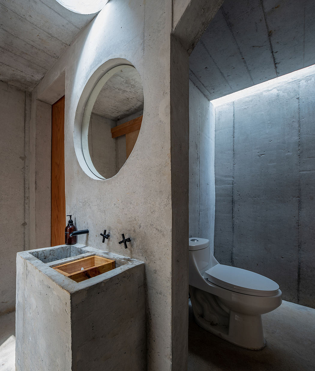 Minimalist bathroom with concrete walls, circular mirror, and wood-framed vanity.