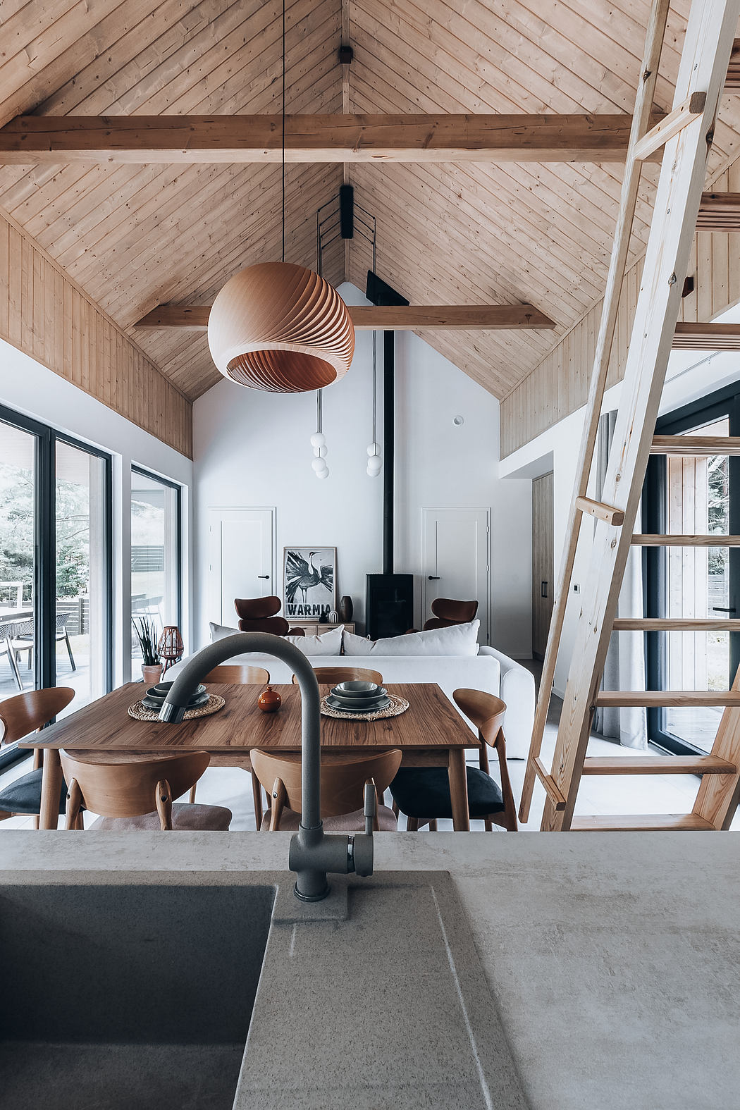 A cozy modern cabin interior with wooden beamed ceilings, sleek furniture, and a central fireplace.