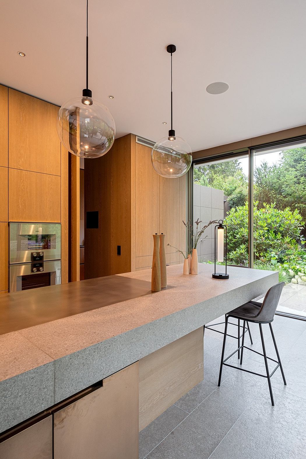 Sleek modern kitchen with pendant globe lights, wood cabinetry, and a concrete countertop.