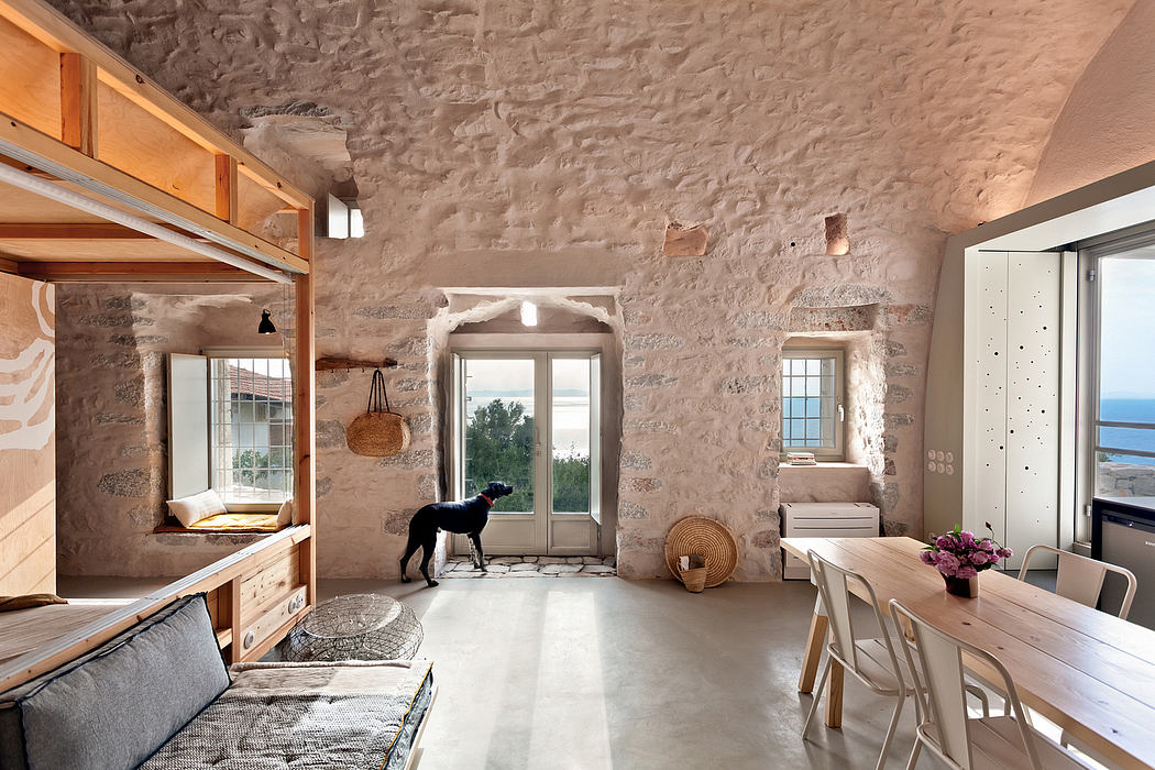 A rustic, open-plan living space with stone walls, wooden beams, and large windows.