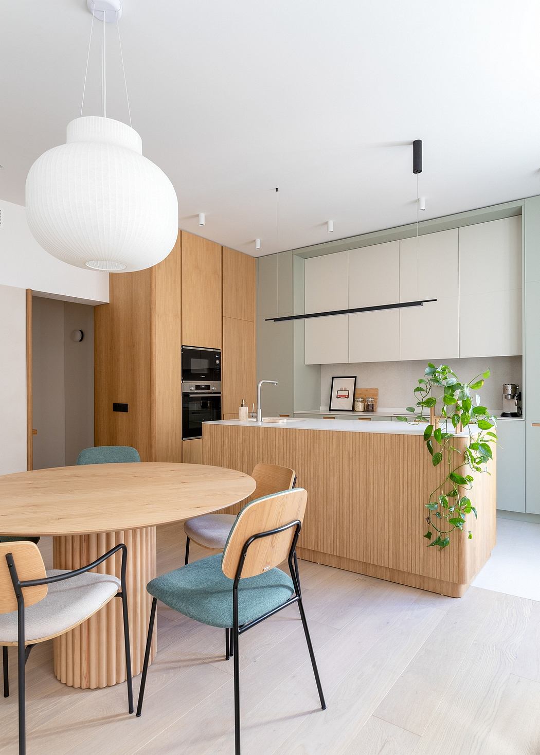 Sleek, minimalist kitchen with light wood cabinets, round dining table, and potted plant.
