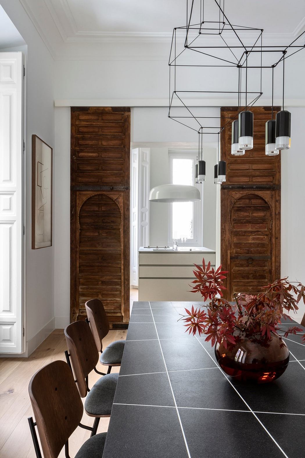 A modern dining room with rustic wooden doors, sleek black furniture, and a striking geometric light fixture.