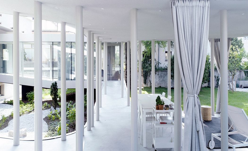 Modern architectural interior with minimalist white columns, large windows, and lush outdoor views.
