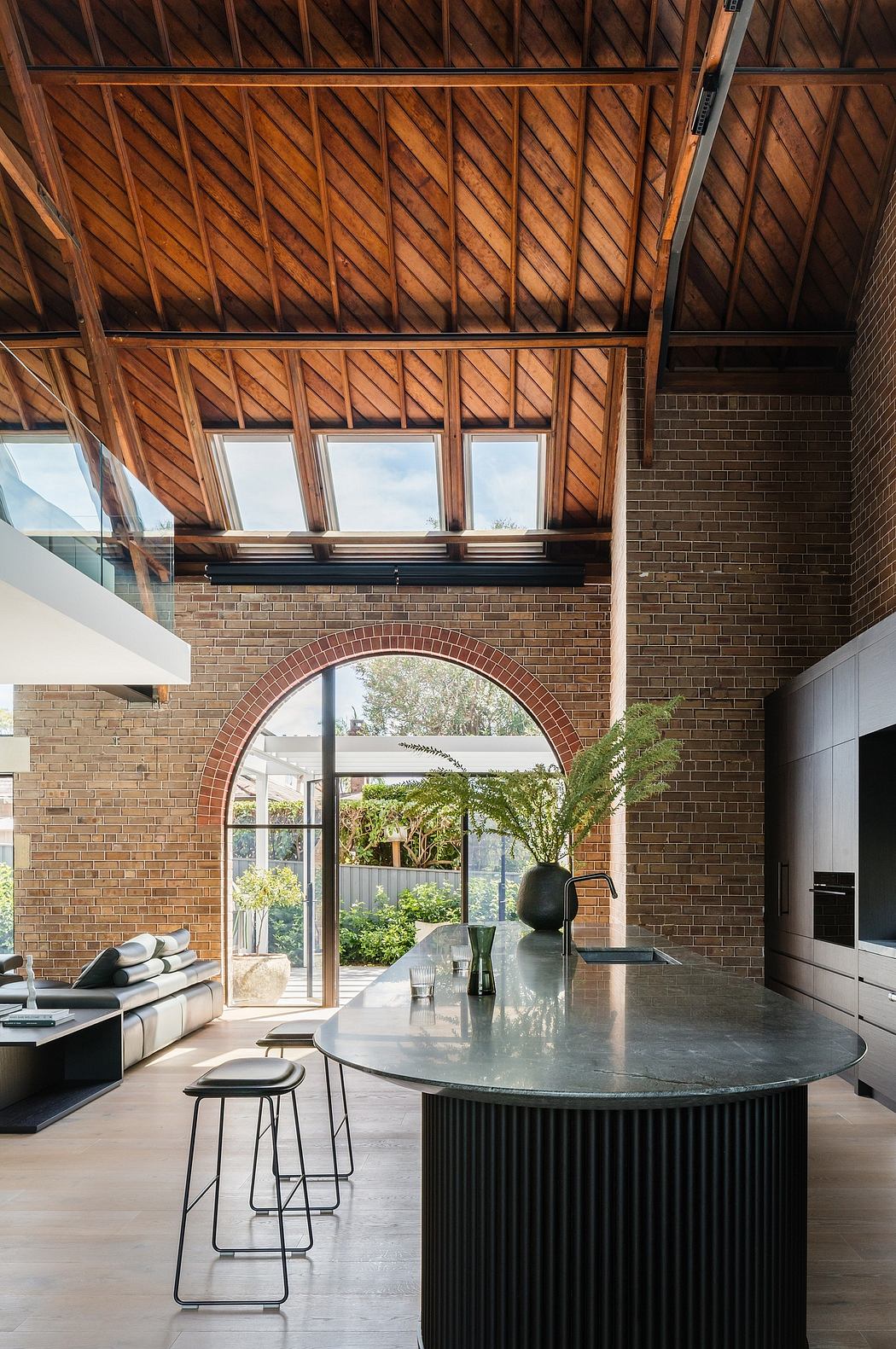 A modern and spacious interior with high ceilings, exposed wooden beams, and a large arched window overlooking greenery.