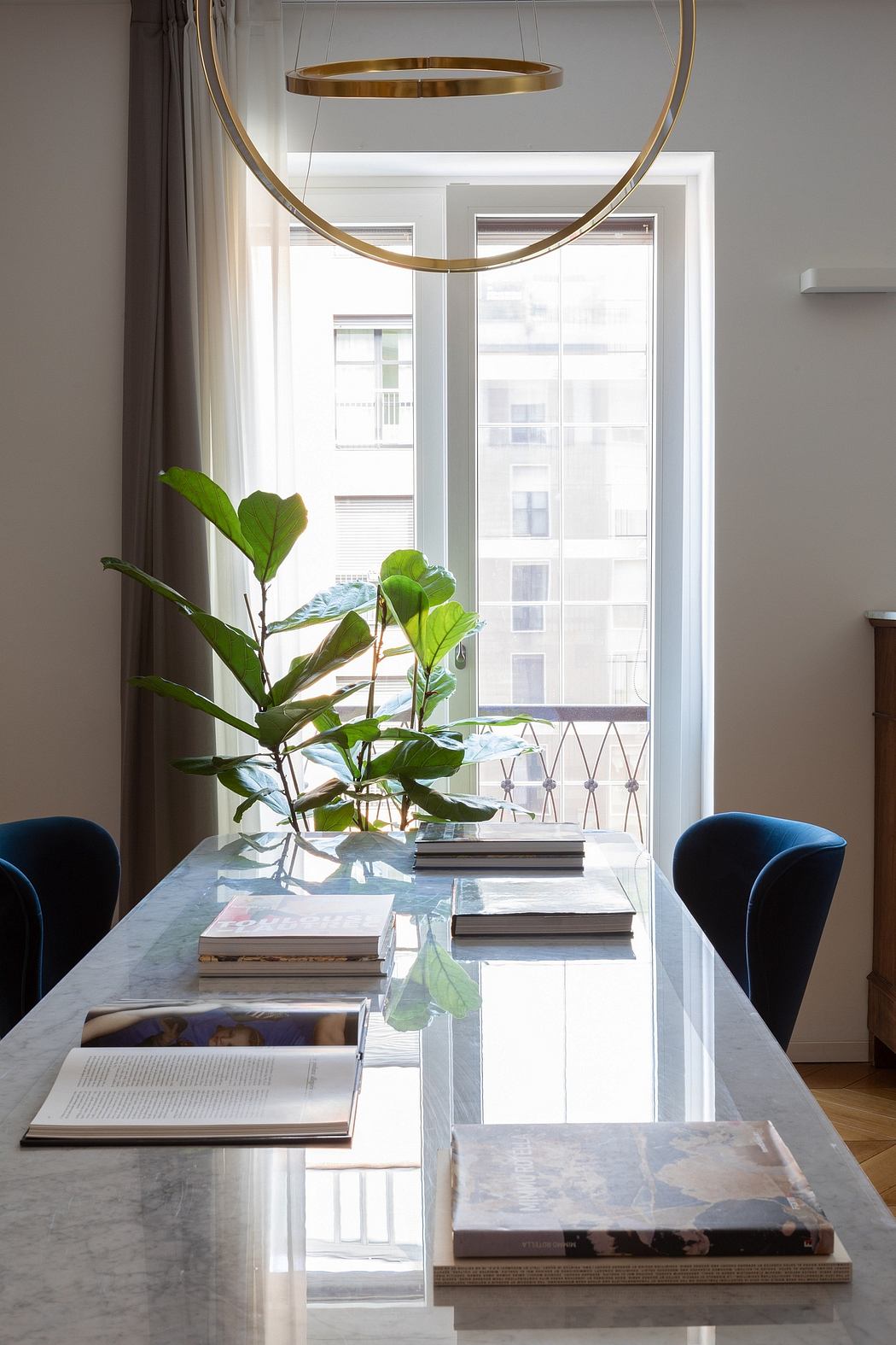 Chic dining space with marble table, gold pendant light, and greenery.