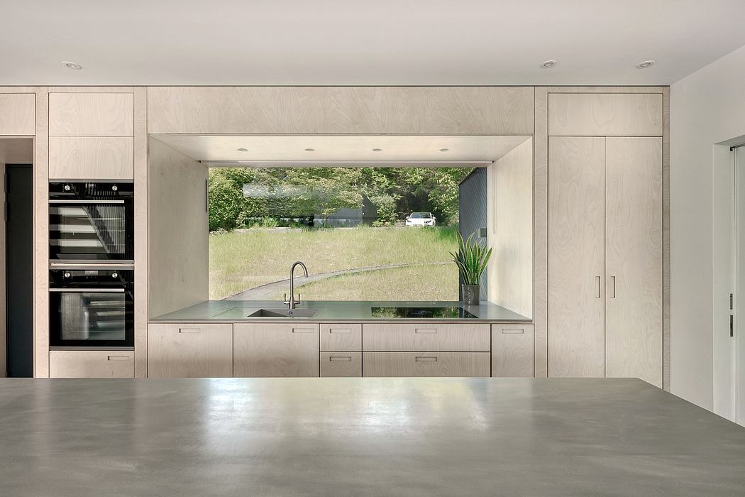 Sleek, minimalist kitchen with floor-to-ceiling window offering scenic outdoor view.