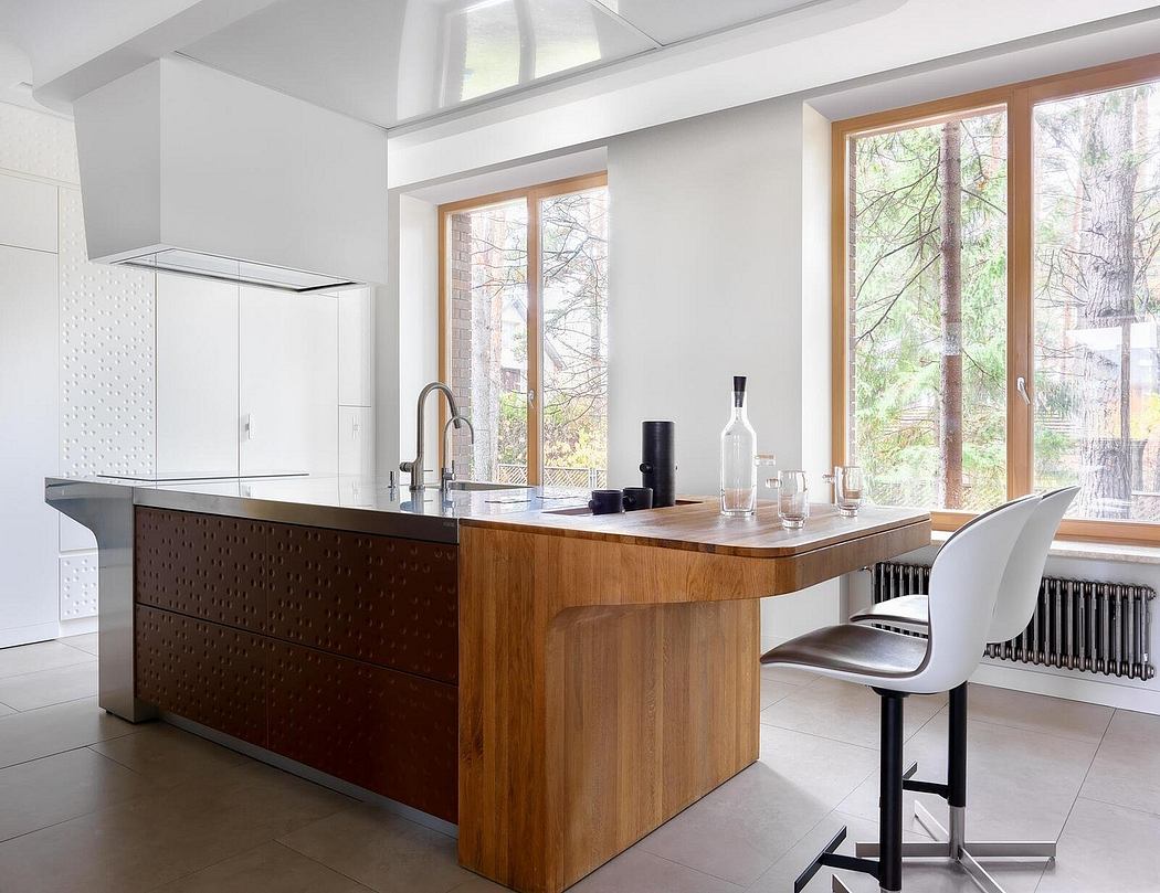 Modern kitchen with wood cabinetry, white walls, and large windows overlooking trees.