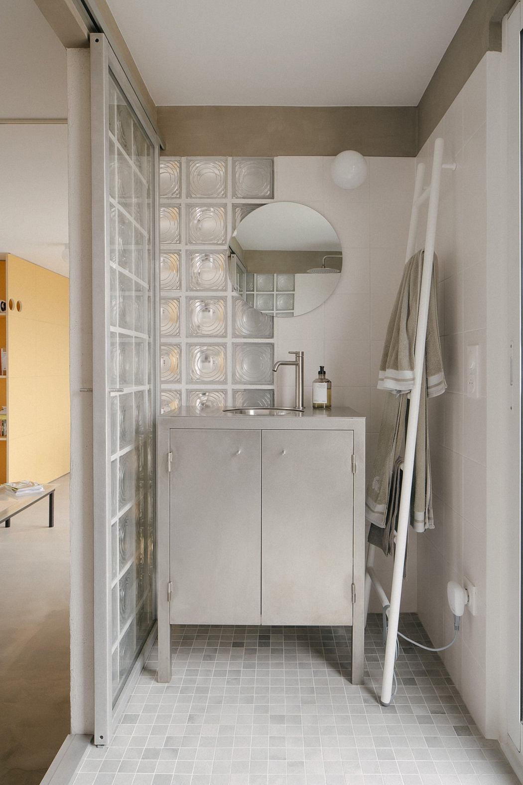 Modern bathroom with glass wall, vanity cabinet, and ladder towel rack.